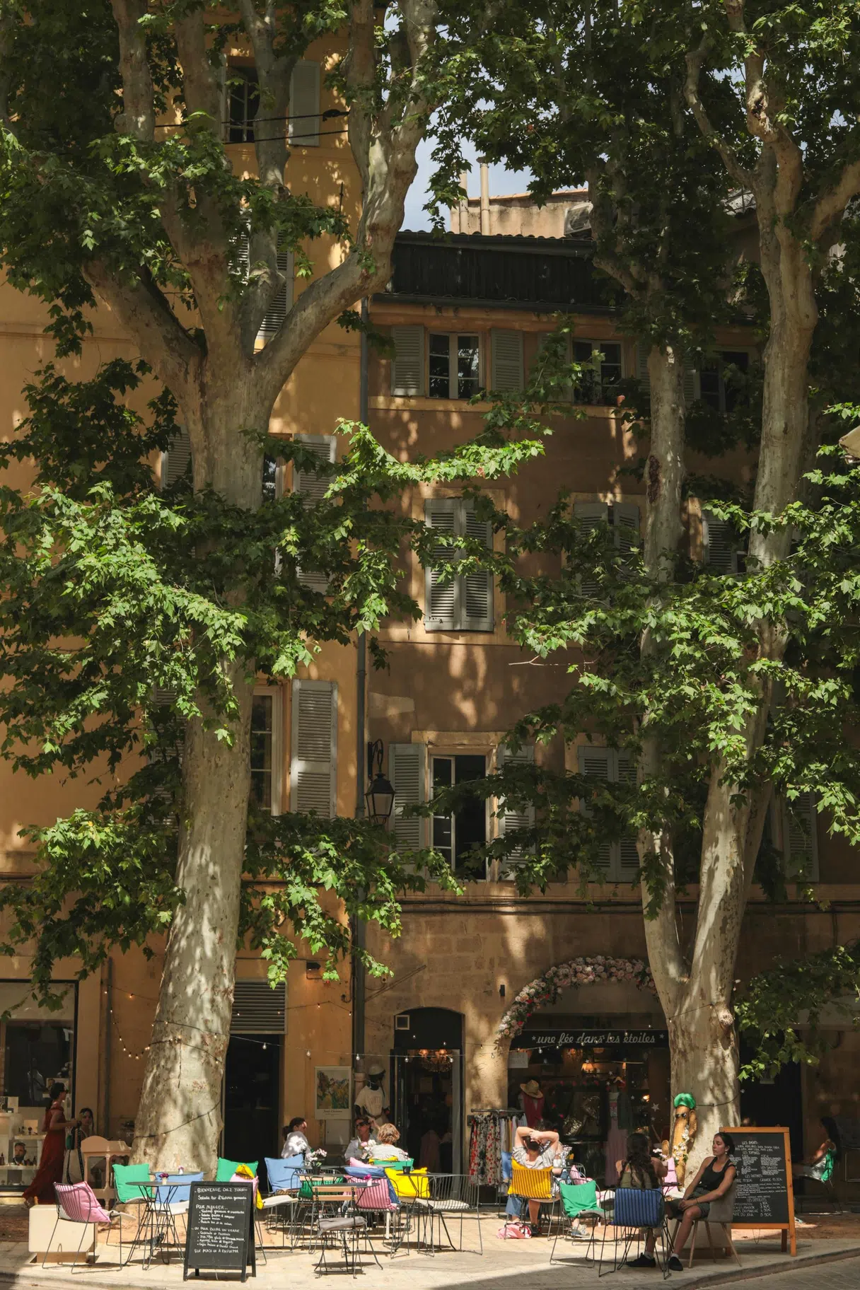 A café terrace beneath plane trees in front of a historic building in Aix-en-Provence